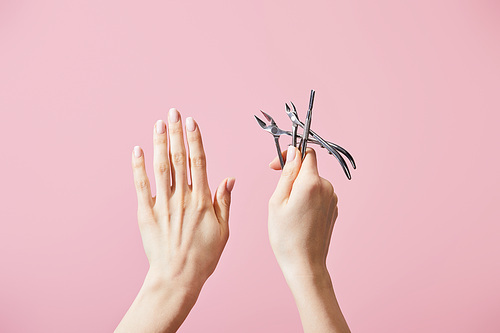 Cropped view of woman holding cuticle pusher and nippers isolated on pink