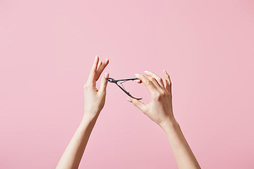 Cropped view of woman cutting cuticle with nipper isolated on pink