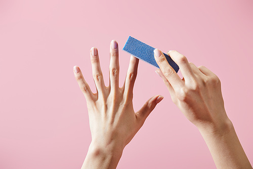 Partial view of woman doing manicure with nail buffer isolated on pink