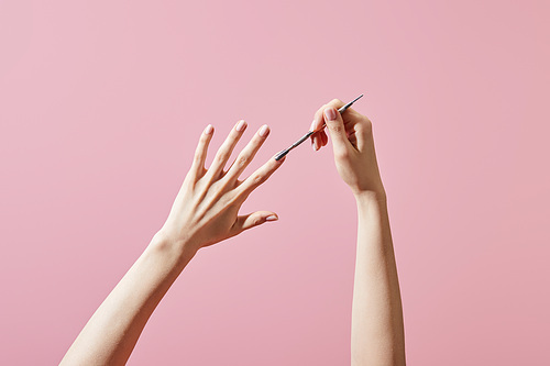 Cropped view of woman doing manicure with cuticle pusher isolated on pink
