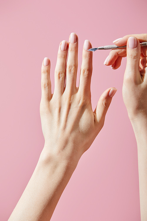 Partial view of woman doing manicure with cuticle pusher isolated on pink