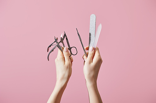 Cropped view of woman holding manicure instruments isolated on pink