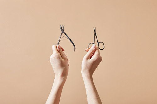 Cropped view of woman holding cuticle nipper and nail scissors isolated on beige