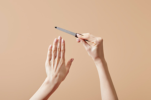 Cropped view of female hands with nail file isolated on beige