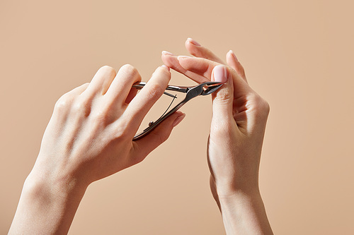 Cropped view of woman doing manicure with cuticle nipper isolated on beige