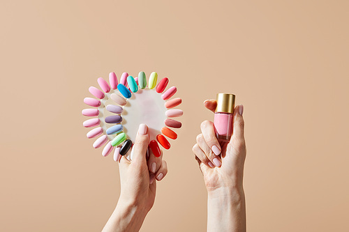Cropped view of woman holding bottle and samples of nail polish isolated on beige