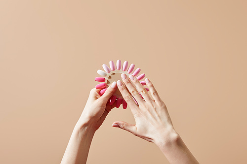 Cropped view of woman holding samples of nail polish isolated on beige