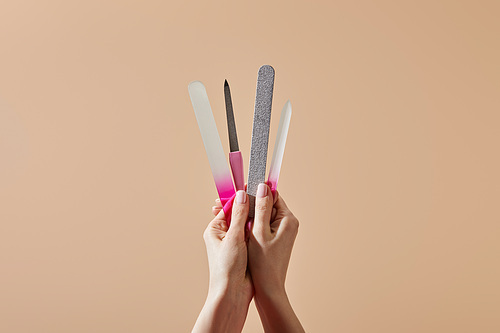 Cropped view of woman holding nail files and emery board isolated on beige