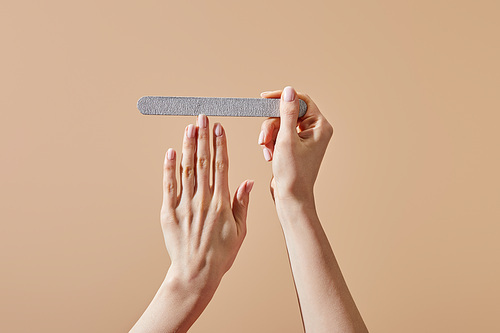 Cropped view of woman filing nail with emery board isolated on beige