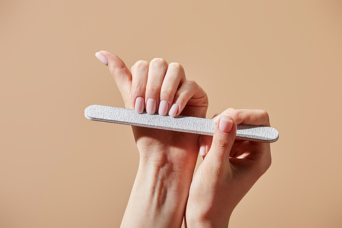 Cropped view of woman filing fingernails with emery board isolated on beige