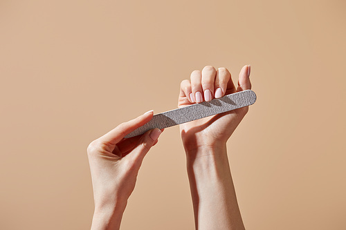 Partial view of woman filing nails with emery board isolated on beige