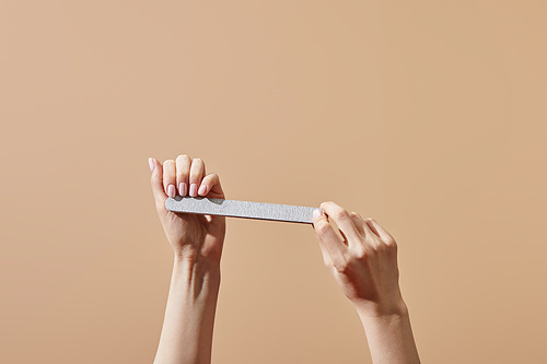 Partial view of woman filing nails using emery board isolated on beige