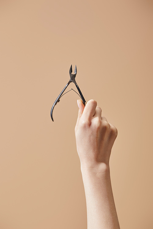 Cropped view of female hand with cuticle nipper isolated on beige