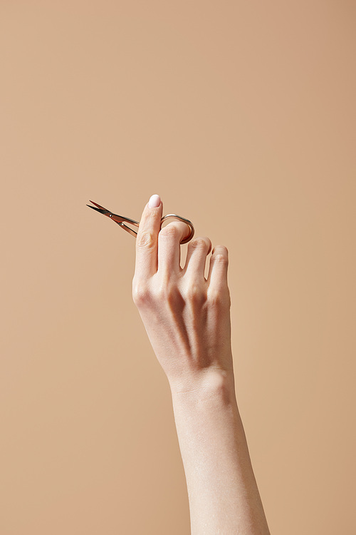 Cropped view of female hand with nail scissors isolated on beige