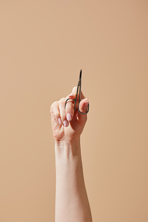 Partial view of female hand with nail scissors isolated on beige