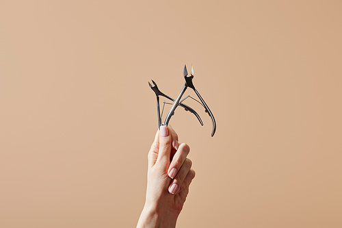 Partial view of female hand with cuticle nippers isolated on beige