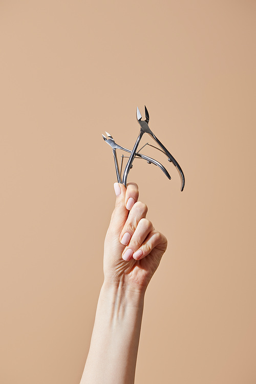 Cropped view of female hand with cuticle nippers isolated on beige