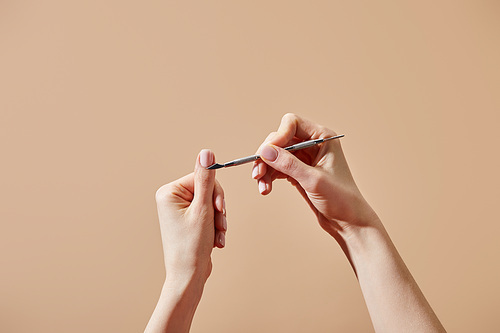 Cropped view of woman doing manicure using cuticle pusher isolated on beige