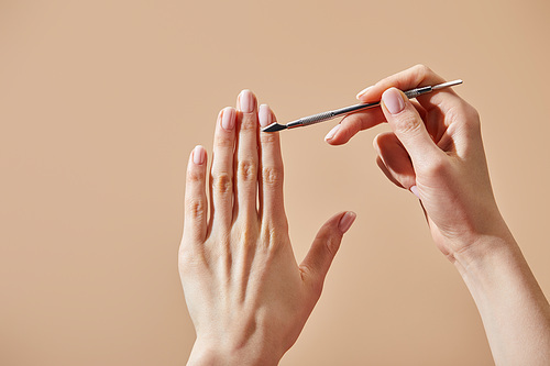 Partial view of woman doing manicure using cuticle pusher isolated on beige