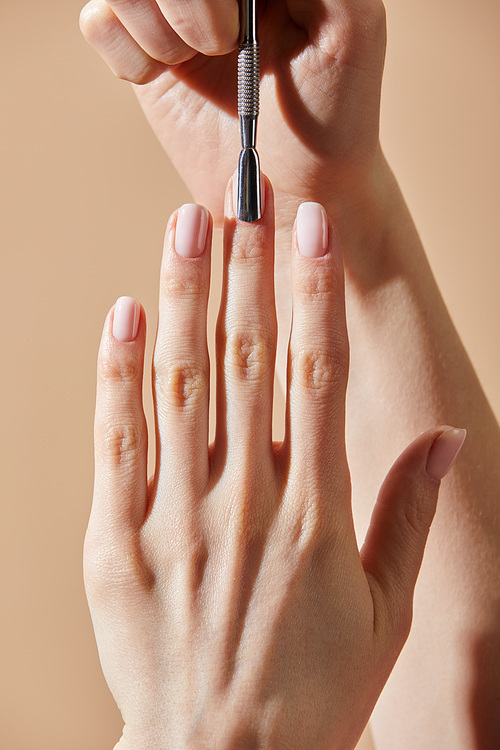 Partial view of woman doing manicure with cuticle pusher isolated on beige