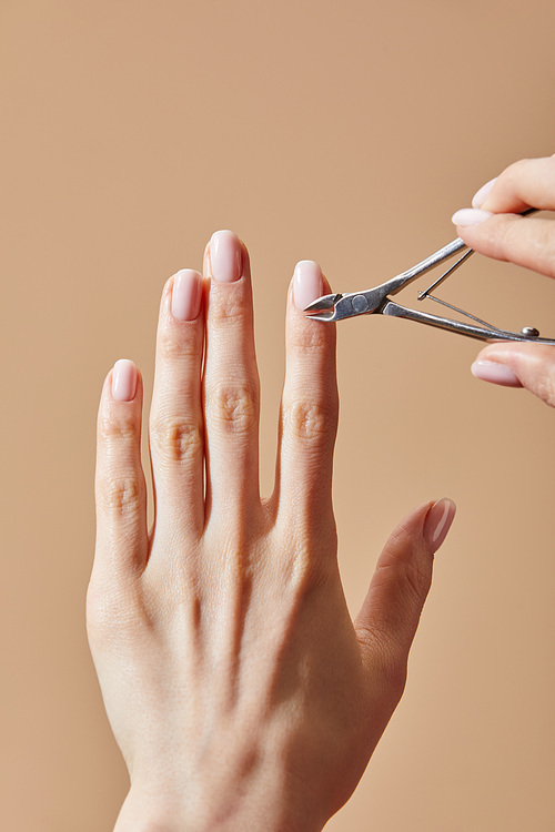 Partial view of woman using cuticle nipper isolated on beige