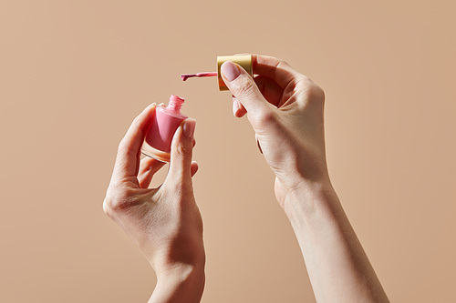 Partial view of woman holding opened bottle of pink nail polish isolated on beige