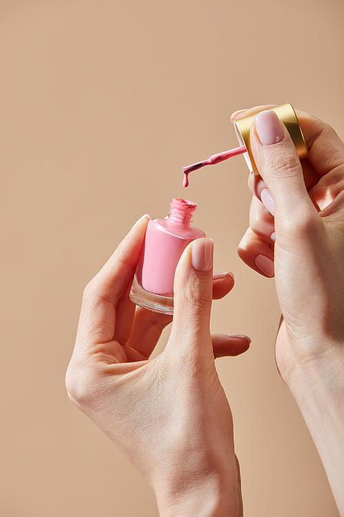 Cropped view of woman holding opened bottle of pink nail polish isolated on beige