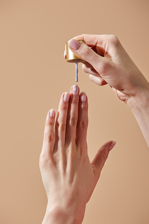 Partial view of woman doing manicure using nail polish isolated on beige