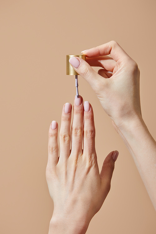 Partial view of woman applying nail polish isolated on beige