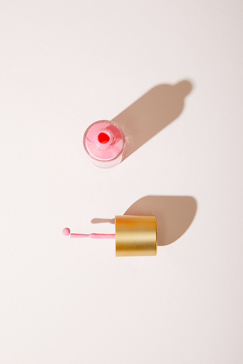 Top view of opened bottle of pink nail polish on white background