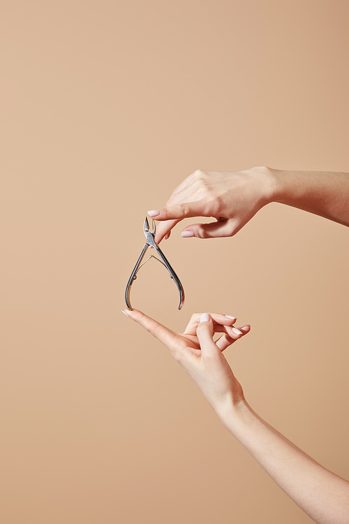 Partial view of woman holding cuticle nipper isolated on beige