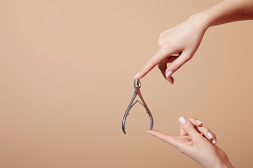Cropped view of woman holding cuticle nipper isolated on beige