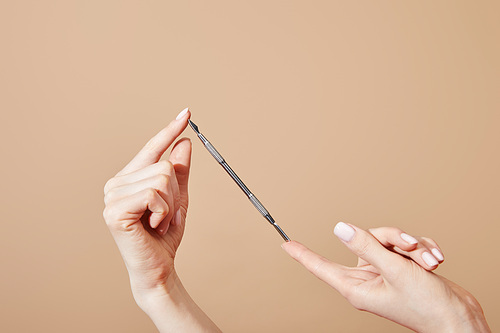 Cropped view of female hands with cuticle pusher isolated on beige