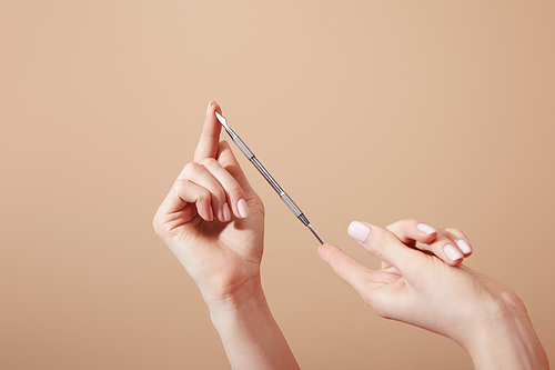 Partial view of female hands with cuticle pusher isolated on beige