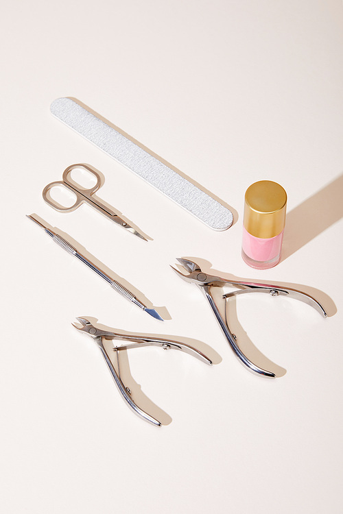High angle view of bottle of pink nail polish with manicure instruments on white background