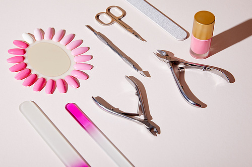 High angle view of bottle and samples of nail polish near manicure instruments on white background