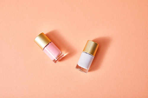 Top view of bottles of pink and white nail polish on coral background