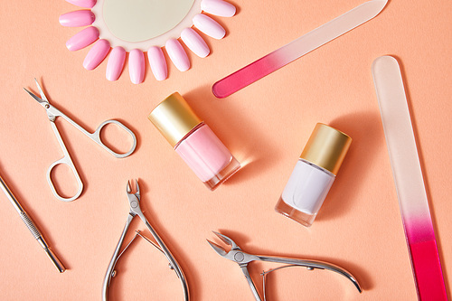 Top view of bottle and samples of nail polish with manicure instruments on coral background