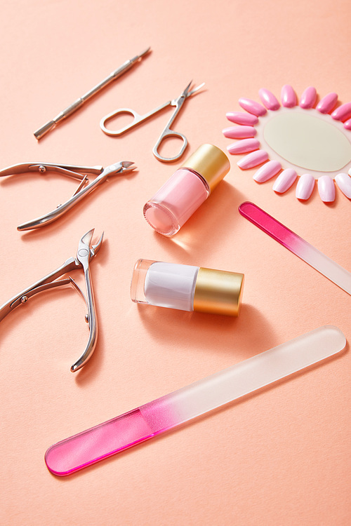 High angle view of bottles and samples of nail polish with manicure instruments on coral background