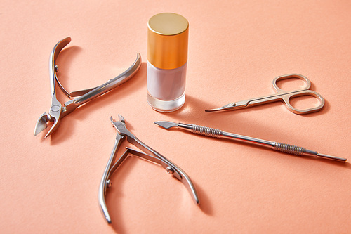 High angle view of bottle of white nail polish with manicure instruments on coral background