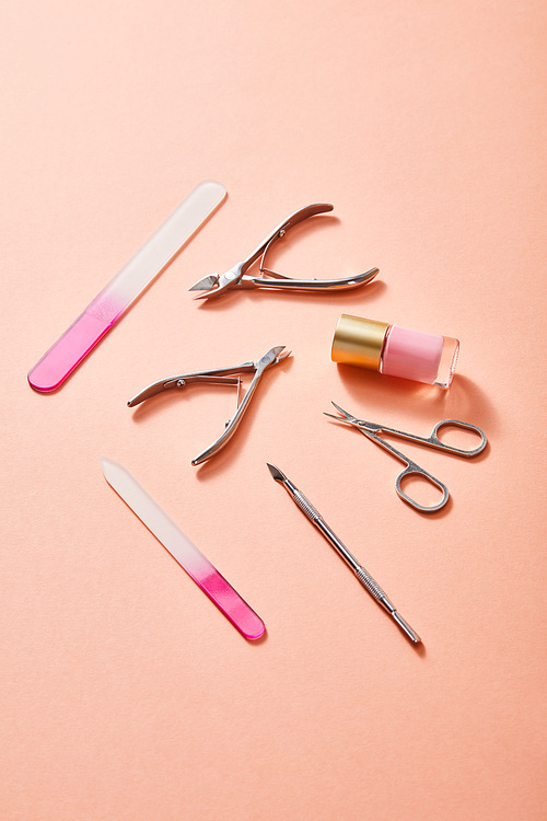 High angle view of bottle of pink nail polish and manicure instruments on coral background
