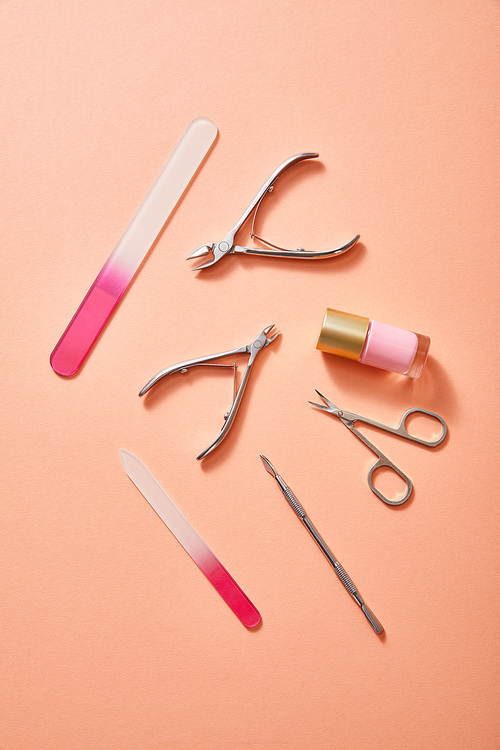 Top view of manicure instruments and bottle of pink nail polish on coral background