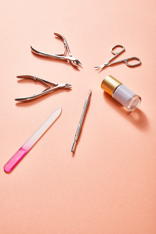 High angle view of bottle of white nail polish and manicure instruments on coral background