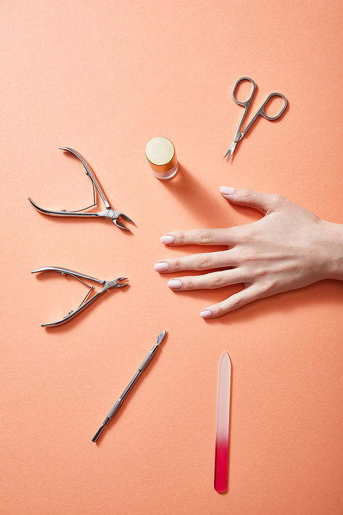 Cropped view of female hand with bottle of nail polish and manicure instruments on coral