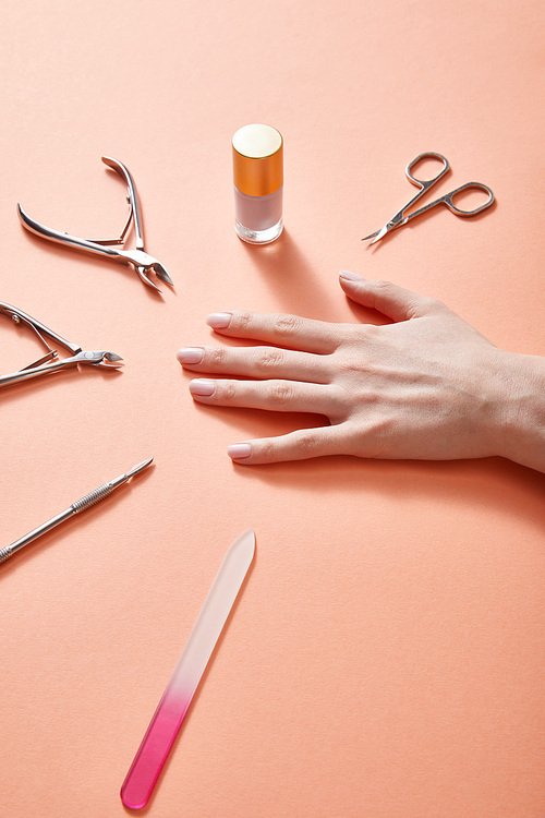 Partial view of female hand with bottle of nail polish and manicure instruments on coral
