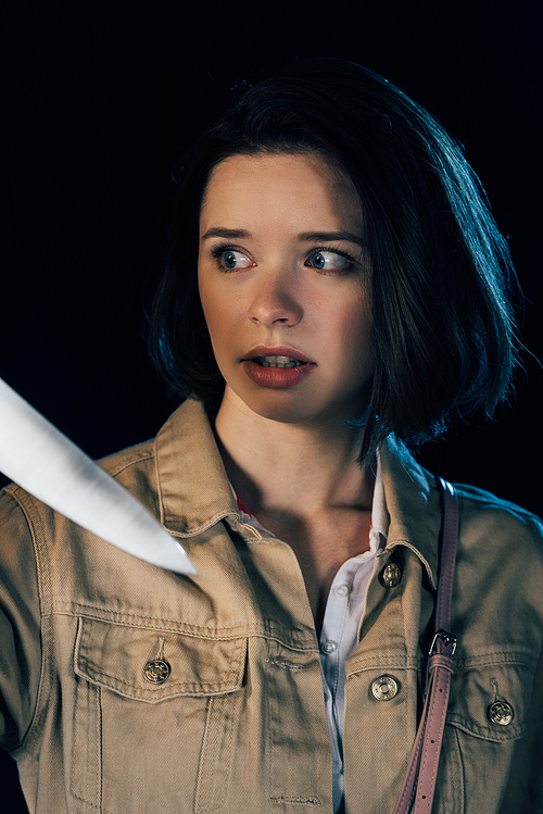 pretty scared woman looking at knife isolated on black