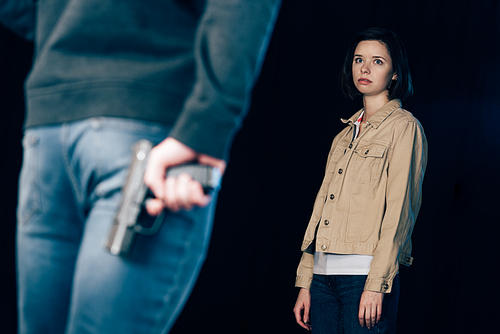 cropped view of criminal hiding gun while standing near woman on black