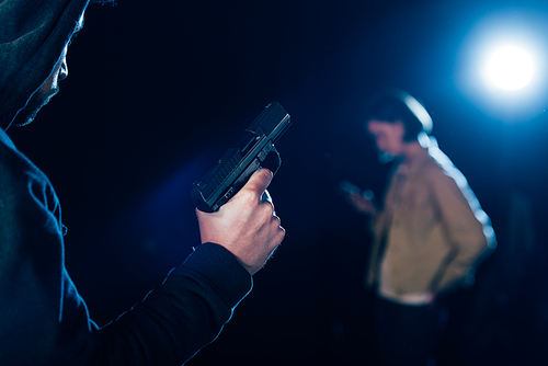 cropped view of killer in hood holding gun and looking at woman on black