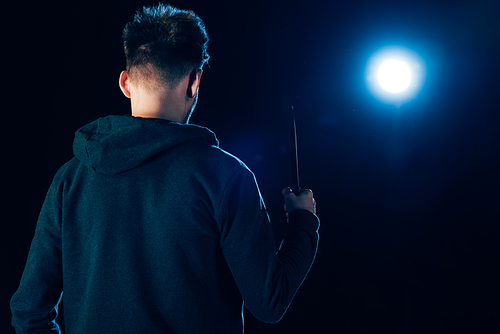 back view of killer holding knife isolated on black