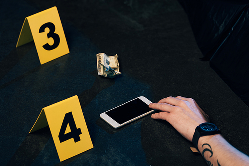 partial view of covered corpse with smartphone and dollar banknote at crime scene